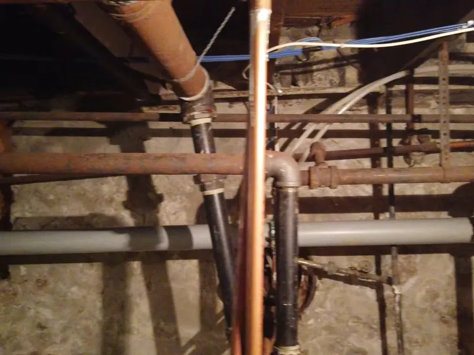 Copper and steel plumbing lines run through an open basement utility area for Maricopa Plumbing Pros